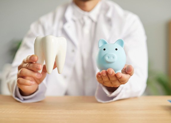 Man in white coat holding large model tooth and small blue piggy bank in either hand