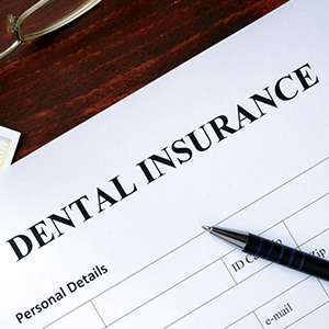 Top of dental insurance form on desk with pen, glasses, money, and X-rays