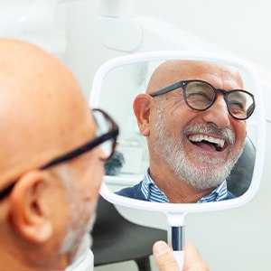 A man smiling in a mirror at his new dental implants