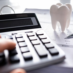 Hands holding pen and pressing buttons on calculator at desk with large model tooth
