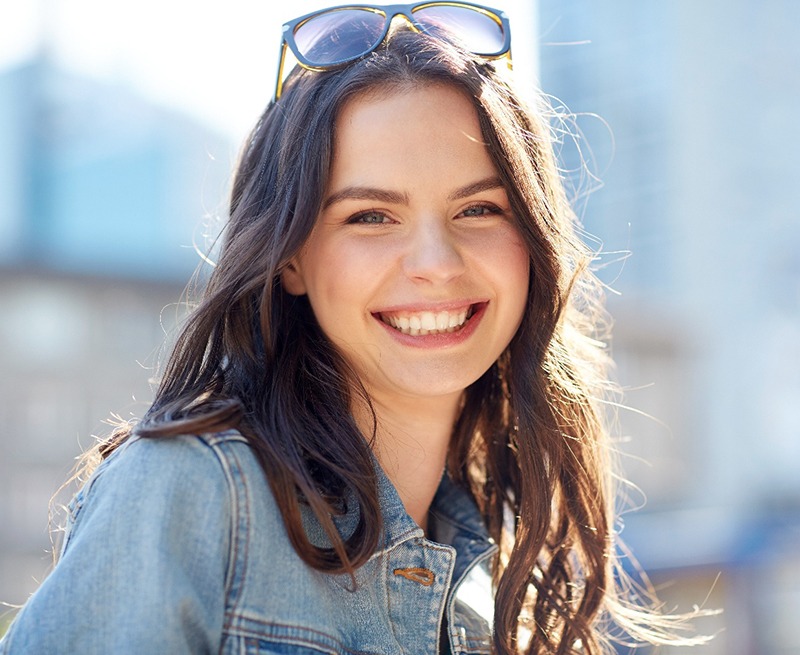 Woman with denim jacket and sunglasses smiling