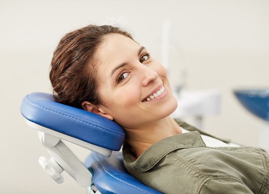 Woman with brown hair leaning back in dental chair and smiling