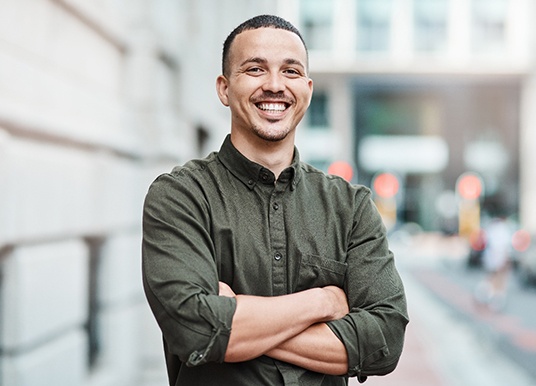 Man smiling with arms folded on sidewalk