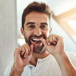 Man smiling while flossing his teeth in bathroom