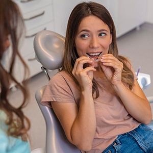 Patient holding clear aligner while looking at dentist at appointment