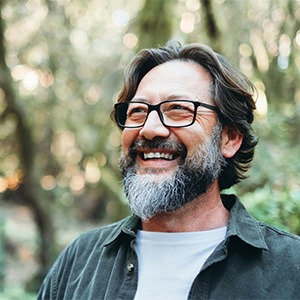 Senior man with glasses and beard smiling outside